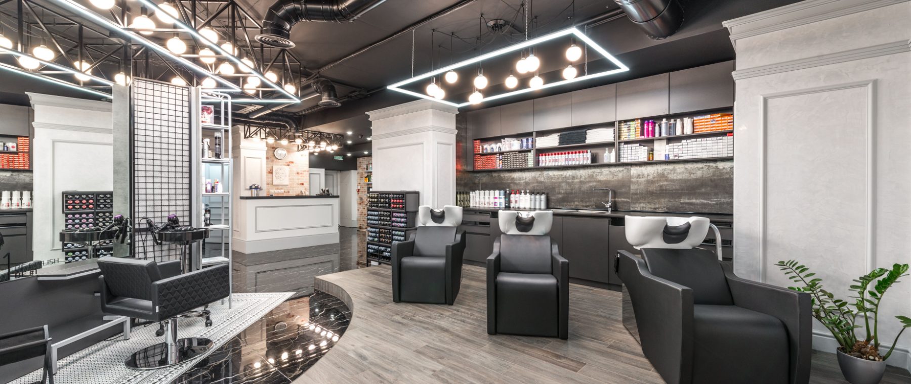 A modern salon floor with styling stations, wash basins and a wall of professional product.